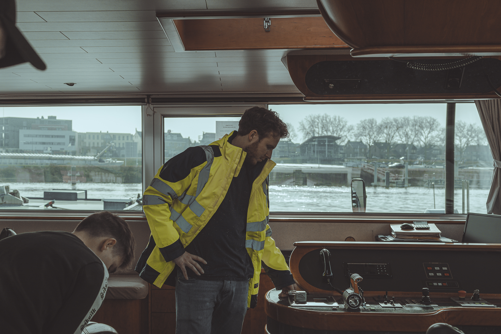 Captain in a hi-vis jacket at the wheelhouse controls of an inland vessel