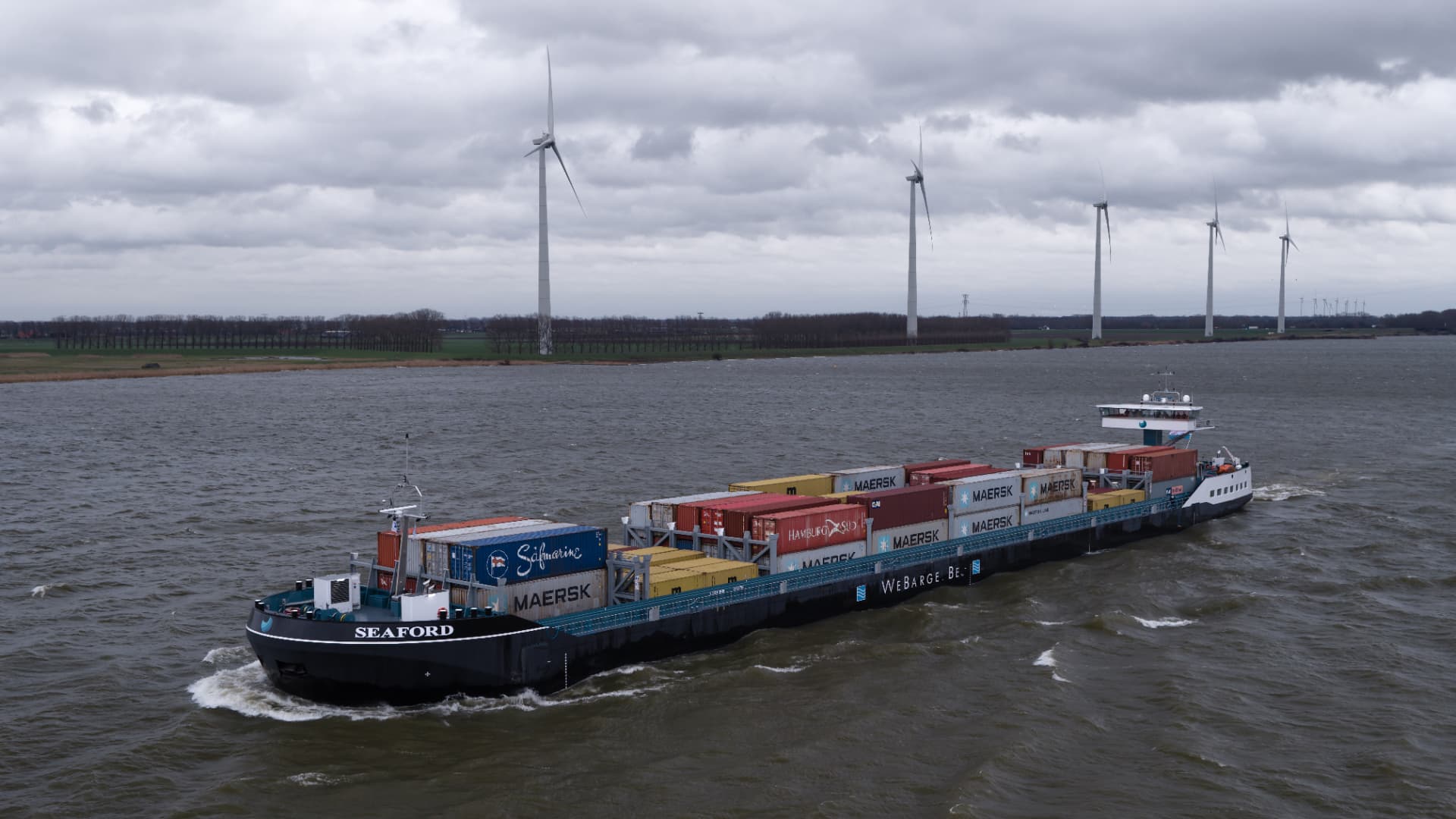 The remotely operated inland container vessel Seaford sailing past wind turbines
