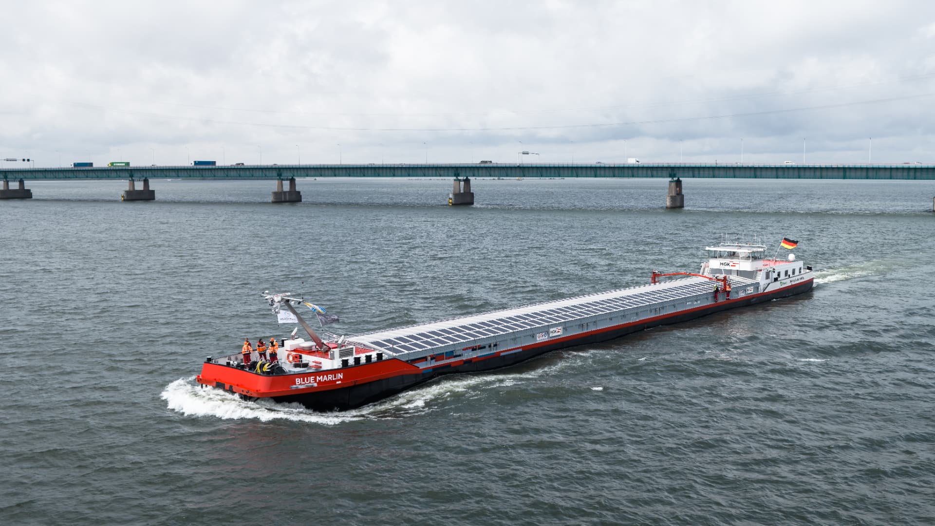 Het binnenschip Blue Marlin van HGK Shipping onderweg, met zonnepanelen op de luiken, onder een snelwegbrug