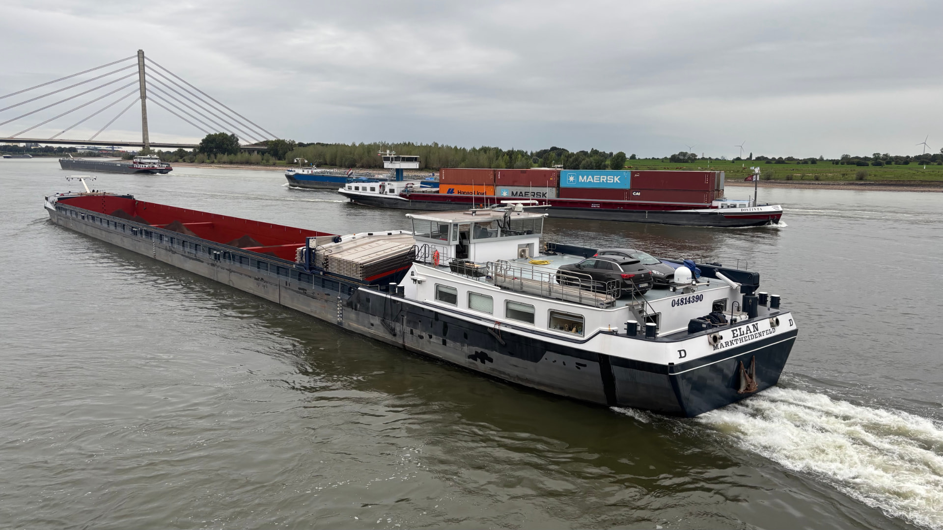 Motor vessel Elan sailing on a busy inland waterway near a cable-stayed bridge