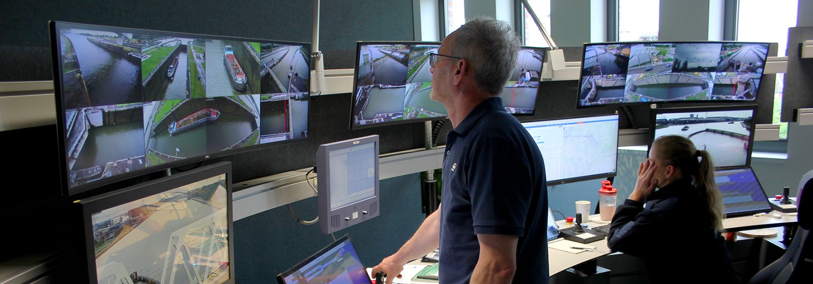 Operator at a De Vlaamse Waterweg remote-control centre monitoring locks and bridges across multiple screens